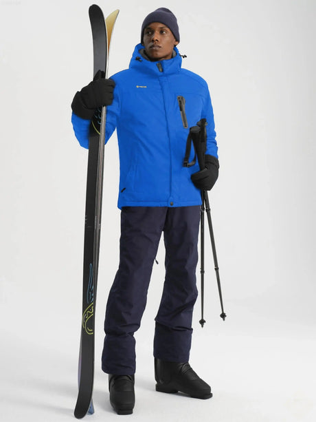 Man wearing blue ski jacket and navy pants holding skis and poles.