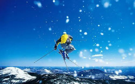 Skier performing a mid-air jump against a snowy mountain backdrop.