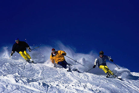 Three skiers racing downhill on snowy slopes.