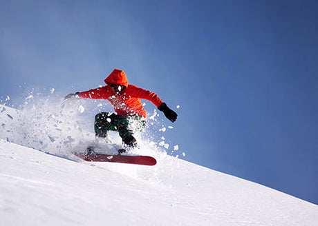 Snowboarder in a bright red jacket carving through powdery snow.