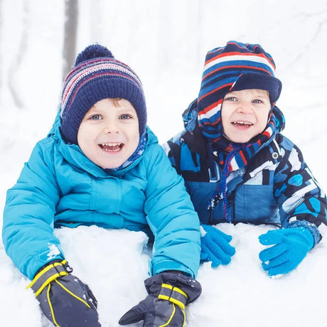 Two young children in kids jackets enjoying winter fun in the snow.