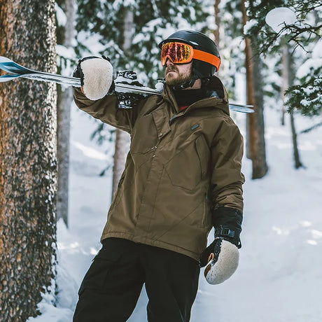 Skier in snowy forest showcasing Gemyse’s men’s jackets while carrying skis.