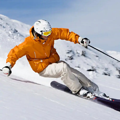 Skier in a bright orange jacket carving down a snowy slope.